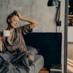 Portrait of young relaxed woman in stylish home suit waking up with cup of coffee in bed